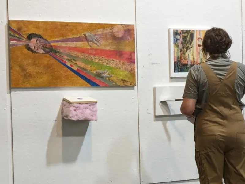 People in a gallery viewing Transreal Objects artworks by Adam Sprague on a white wall.